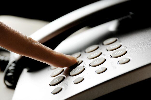 Foto dedo pressionando o botão numérico no telefone para fazer uma chamada de perto