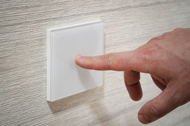 Un dedo de primer plano enciende la luz del interruptor táctil. Un interruptor de luz moderno blanco sobre una pared blanca. diseño moderno.