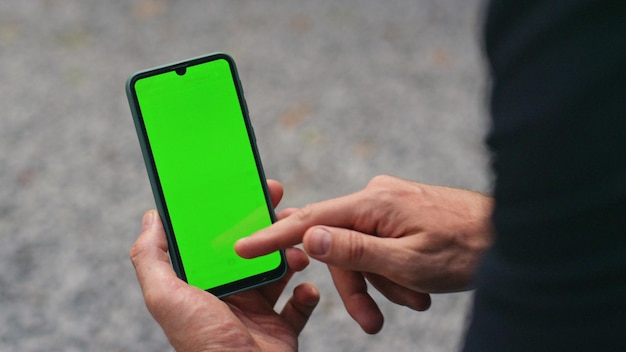 Un dedo de primer plano tocando la pantalla verde de un teléfono inteligente con la mano sosteniendo un dispositivo celular de maqueta