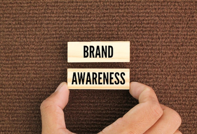 Foto dedo segurando uma placa de madeira com a palavra brand awareness o conceito de brand awareness
