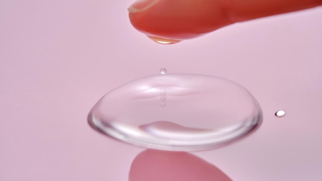 Un dedo toca una gota de producto cosmético sobre un fondo rosado