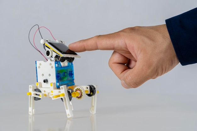 Un dedo toca un panel solar encima de un robot de juguete hecho de envases de plástico Concepto educativo de tecnología sostenible Aprender en la innovación cosas nuevas desarrollo continuo