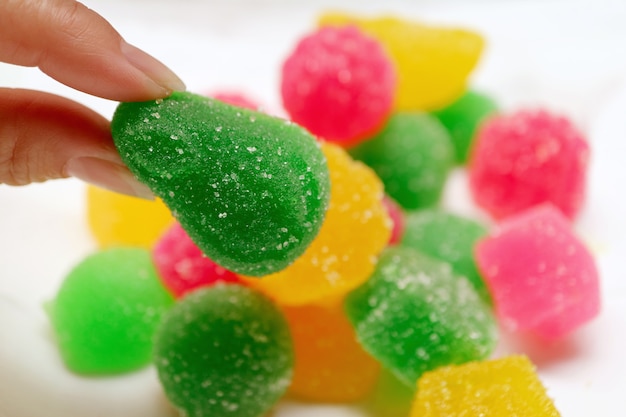 Dedos de mulher pegando balas de gelatina cobertas de açúcar verde vibrante da pilha de balas