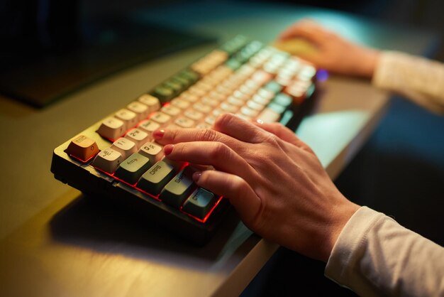Los dedos de las manos de los jugadores profesionales en línea teclado mecánico en fondo borroso de color neón