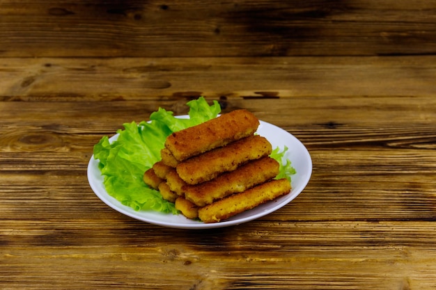 Dedos de pescado frito en un plato con lechuga en la mesa de madera