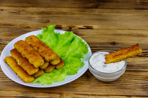 Dedos de pescado frito en un plato con lechuga y salsa tártara en la mesa de madera