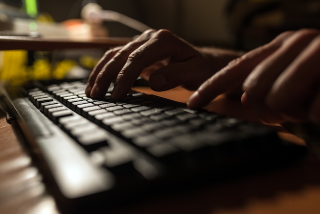 Dedos pressionando um teclado de computador no escuro.