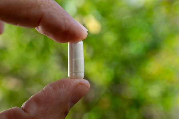 Dedos segurando cápsula de medicamento manipulada, com fundo verde