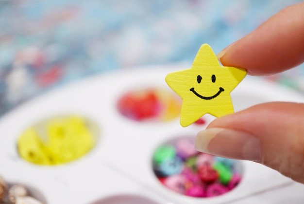 Los dedos sosteniendo una perla de madera de la Estrella Sonriente para hacer accesorios de perlas