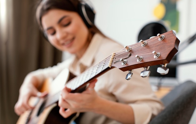 Defokussierte Musikerin, die zu Hause Akustikgitarre spielt