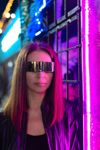 Defokussierte schöne junge Frau in kosmischer Brille, die neben buntem Neonlicht steht