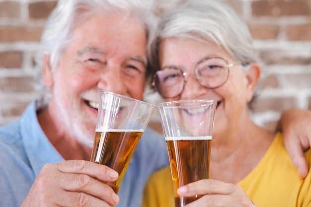 Defokussiertes älteres lächelndes Paar, das mit einem Glas blondem Bier röstet