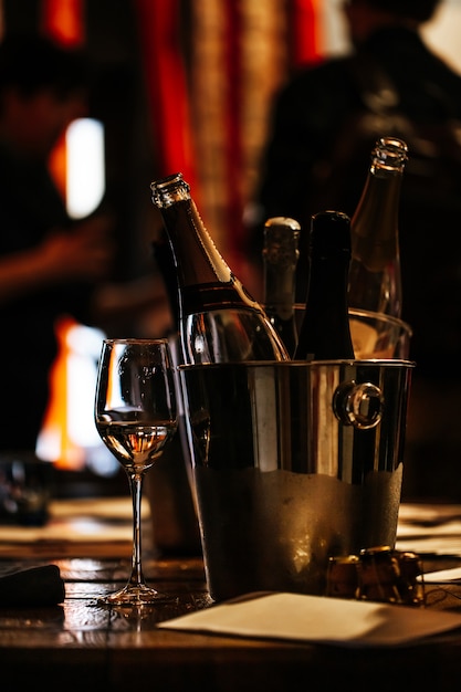 Degustação de vinhos: em uma mesa de madeira há um balde de prata para refrigerar vinhos com garrafas abertas de champanhe e uma taça de vinho.
