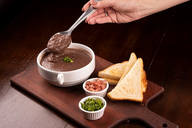 Degustación de una cucharada de caldo de frijol con primer plano y condimentos en primer plano de madera de cebollino tocino totora