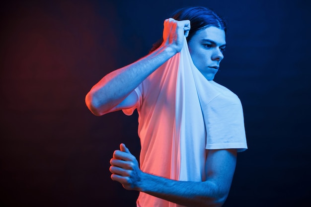 Dehnen Sie es auf. Studioaufnahme im dunklen Studio mit Neonlicht. Porträt des ernsten Mannes.
