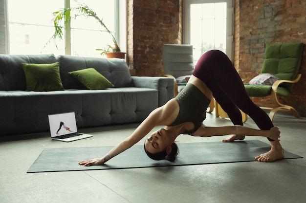 Dehnen. Sportliche schöne junge Frau, die zu Hause Yoga-Asanas wie Profi praktiziert.