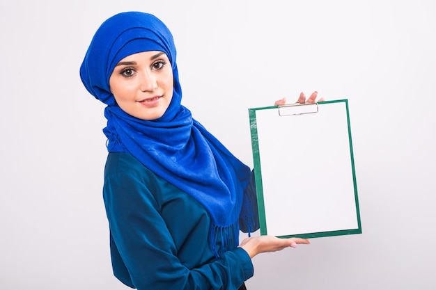 Dein Text hier. Recht junge aufgeregte arabische Frau, die leeres leeres Brett hält. Buntes Studioporträt mit weißem Hintergrund.