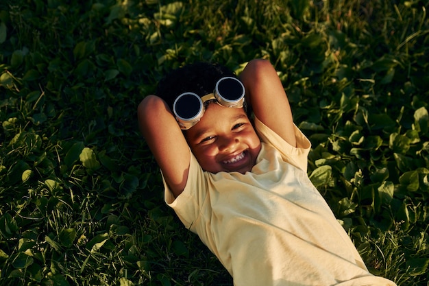 Deitado na grama, criança afro-americana se diverte no campo no dia de verão