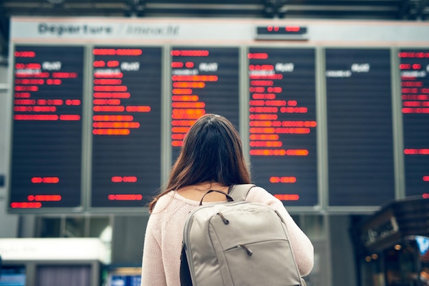 Deixe a jornada começar Captura retrovisora de uma jovem irreconhecível olhando para um quadro de chegadas e partidas enquanto está em um aeroporto