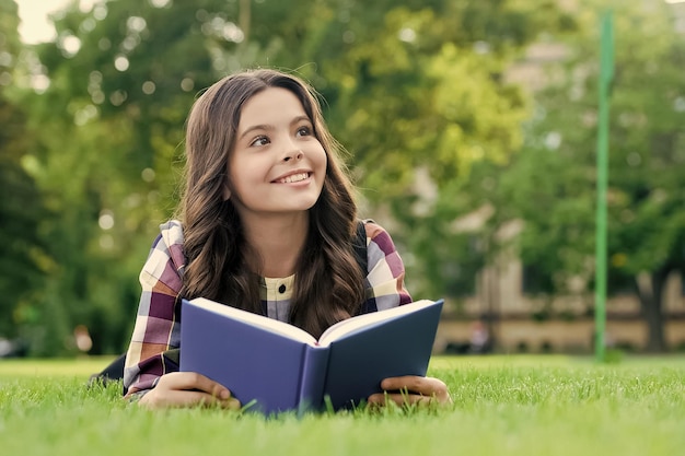 Deixe sua capacidade criativa investigar criança feliz lendo livro deitado na grama verde educação de leitura aprendizagem de livros biblioteca escolar lição de literatura imaginação e fantasia dia do conhecimento | Foto