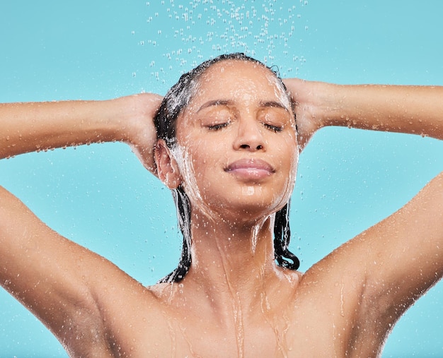 Deja que el agua te lave. Una foto de una mujer joven que se lava el pelo en la ducha con un fondo azul.