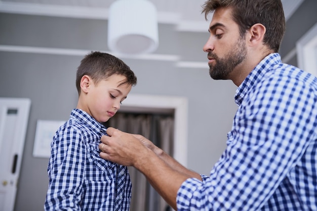 Foto déjame ayudarte con ese botón captura recortada de un apuesto joven y su hijo vistiéndose por la mañana