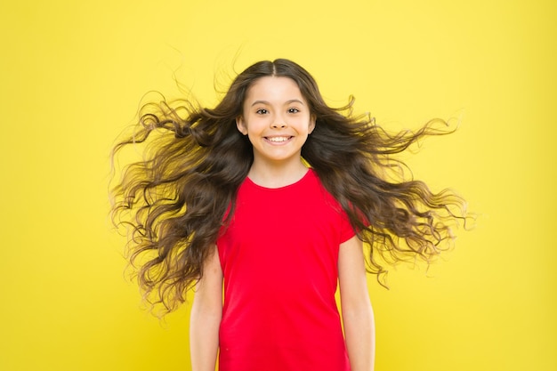 Dejé que mi cabello se fuera. Niño feliz con cabello suelto sobre fondo amarillo. Niño con linda sonrisa y cabello ondulado con textura. Adorable niña sonriente con cabello largo morena.