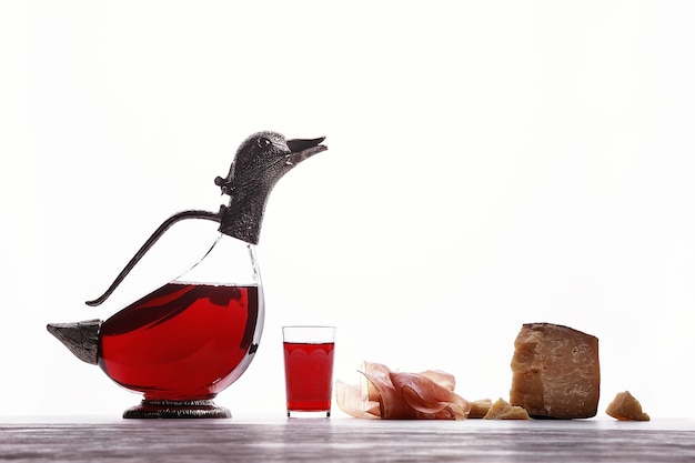 Dekanter mit Wein in Form von Enten, Glas mit Wein, Parmaschinken und teurem Blauschimmelkäse. Auf weißem Hintergrund.