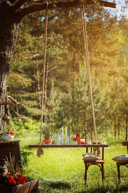 Dekor Romantisches Abendessen mit Kerzen, Blumen im grünen Wald bei herrlichem Sonnenuntergang.