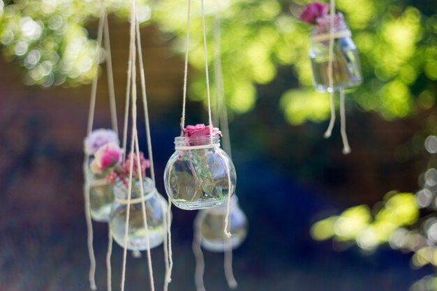 Dekorationsglas mit Blumen, die mit unscharfem Gartenhintergrund hängen. Weicher Fokus