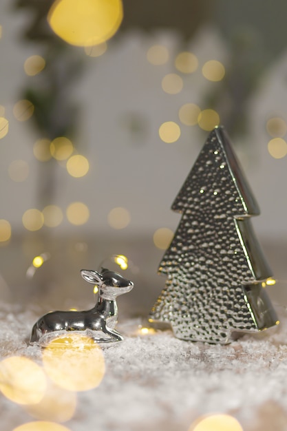 Dekorative Figuren eines Weihnachtsthemas. Statuette eines Lügenrotwilds nahe einem Weihnachtsbaum. Festliches Dekor, warme Bokeh-Lichter.