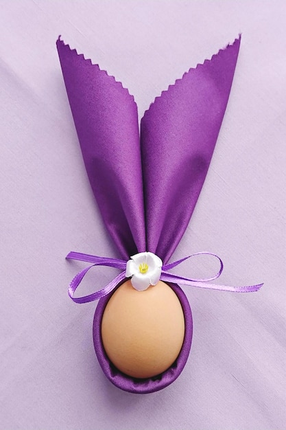 Dekorative Hasenohren mit Ei auf lila Baumwolltischdecke, um Ostern zu feiern