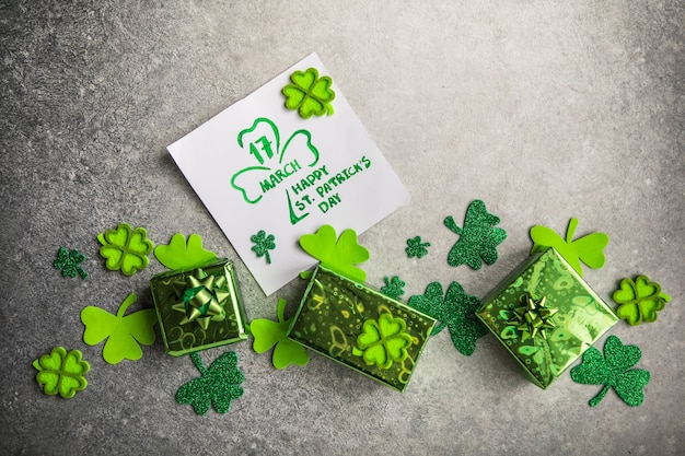 Dekorative Kleeblätter, grüne Geschenkbox, Münzen auf Steinhintergrund, flache Lage. Feier zum St. Patrick's Day. Karte Happy St. Patrick's Day