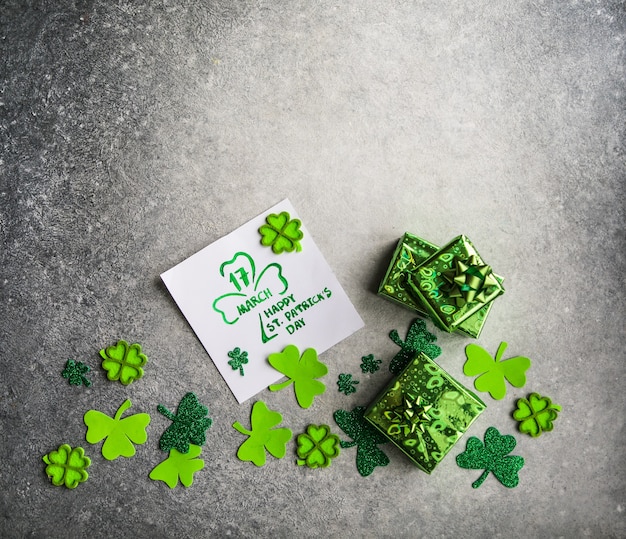 Dekorative Kleeblätter, grüne Geschenkbox, Münzen auf Steinhintergrund, flache Lage. Feier zum St. Patrick's Day. Karte Happy St. Patrick's Day