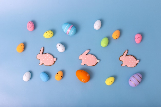 Foto dekorative mehrfarbige eier und rosa lebkuchen in form eines kaninchen auf blauem hintergrund