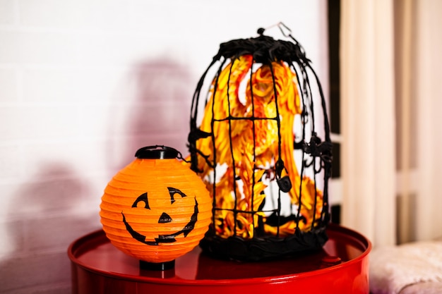 Dekorative Papierkürbislaterne und -käfig mit orange Spielzeugvogel. Dekor für die Feier von Halloween