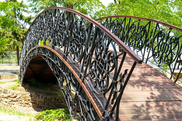 Dekorative schmiedeeiserne Holzbrücke über den Fluss der Steine im Park.