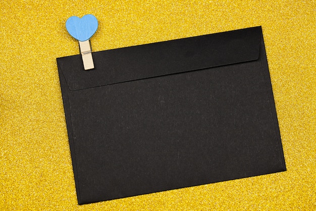 Dekorative Wäscheklammer mit Herzen und schwarzem Umschlag auf gelber Oberfläche