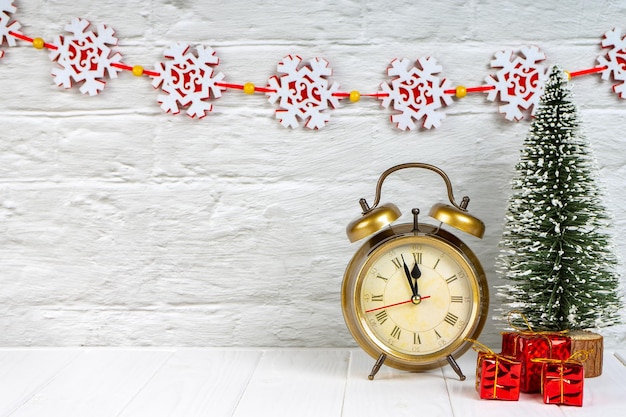 Dekorative Weihnachtsbaum-Geschenkboxen und Wecker auf weißem Holzhintergrund