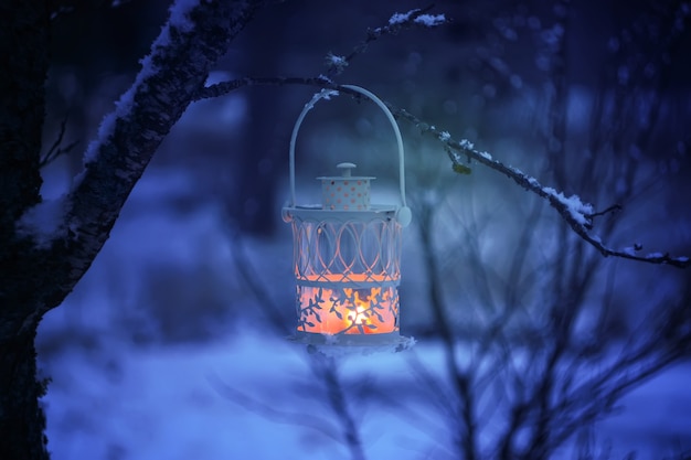 Dekorative Weihnachtslaterne mit brennender Kerze, die an einem schneebedeckten Tannenzweig in einem Winterpark hängt. Festliche Karte des neuen Jahres, Plakat, Postkartendesign.