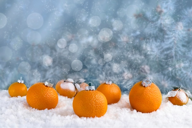 Dekorative Zusammensetzung von Weihnachtsdekorationen gemacht von den Mandarinen auf weißem Schnee. Abstrakter blauer Hintergrund mit Lichtern und Schnee