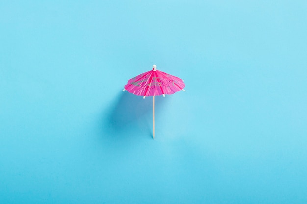 Dekorativer Regenschirm für einen Cocktail auf blauem Hintergrund. Flache Lage, Draufsicht