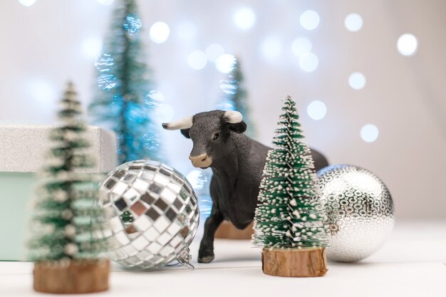 Foto dekorativer stier, symbol des neuen jahres auf dem hintergrund von weihnachtsbäumen und blauem bokeh.