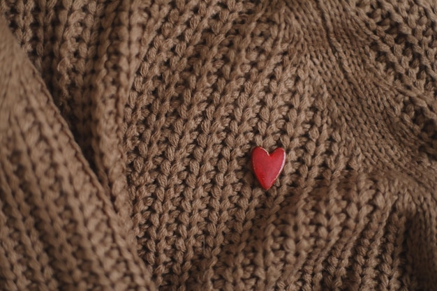 Dekoratives rotes herz auf beige gestricktem texturhintergrund valentinstagfeier oder liebeskonzept