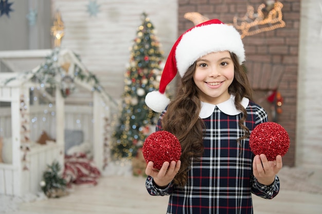 Dekorieren ihrer Lieblingsbeschäftigung. Dekor-Shop. Wählen Sie Dekorationen nach Hause. Kind schmückt Weihnachtsbaumkugeln. Mädchenkind, das Weihnachtsbaum verziert. Kinder-Sankt-Hut, der Weihnachtsbaum schmückt. Festliche Stimmung.