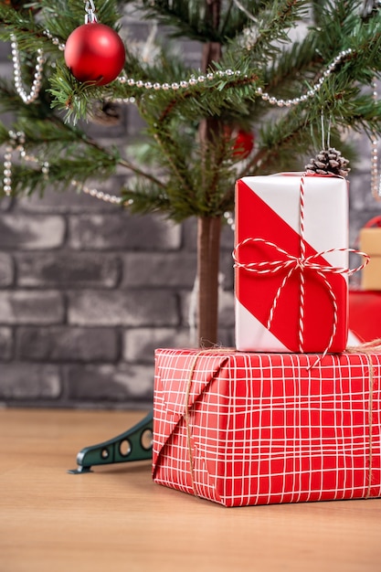 Dekorierter Weihnachtsbaum mit eingewickelten schönen roten und weißen Geschenken zu Hause mit schwarzer Backsteinmauer