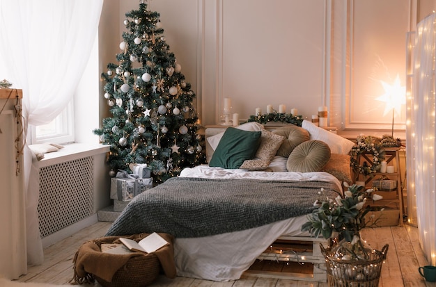 Dekoriertes Zimmer für den Winterurlaub mit einem großen Fenster, einem Weihnachtsbaum und einem weißen Bett in der Nähe