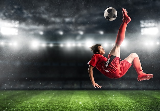 Foto delantero de fútbol en uniforme rojo golpea la pelota con una patada acrobática en el aire en el estadio