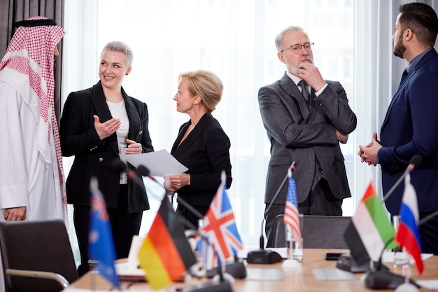 Delegados interculturales discutiendo puntos del discurso de su colega, reunión multiétnica en una moderna sala de juntas, todos vestidos de forma formal, compartiendo opiniones