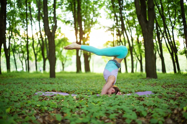 Delgada chica morena practica deportes y realiza posturas de yoga en un parque de verano al atardecer